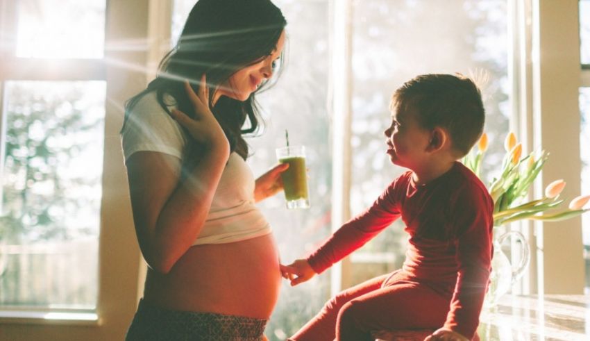 A pregnant woman holding a child in front of a window.