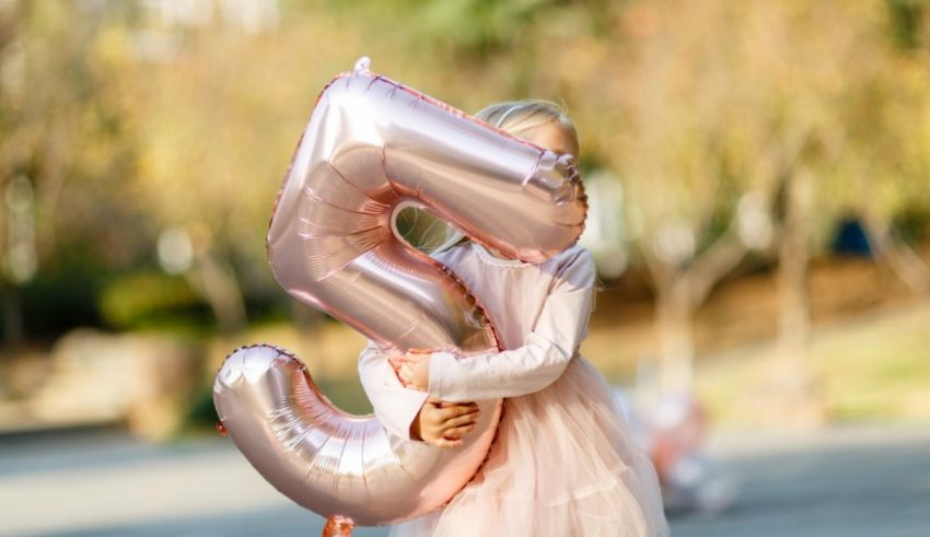 A girl in a pink dress holding a number balloon.