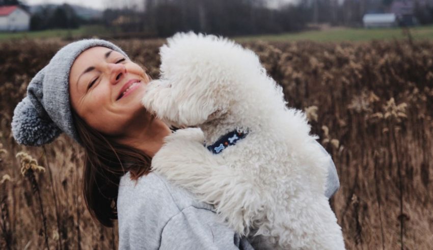 Woman hugging a white poodle in a field.