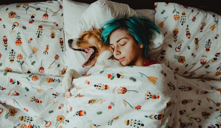 A woman with blue hair and a dog sleeping in bed.