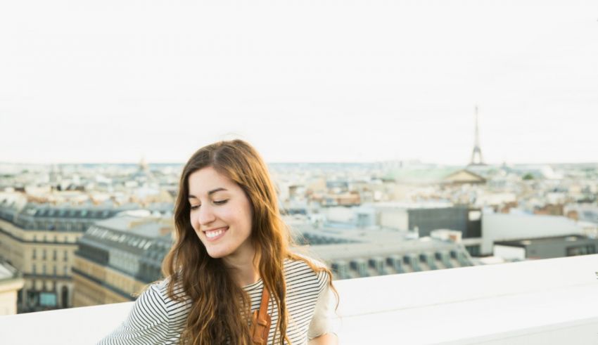 A young woman smiles while standing on a rooftop in paris.
