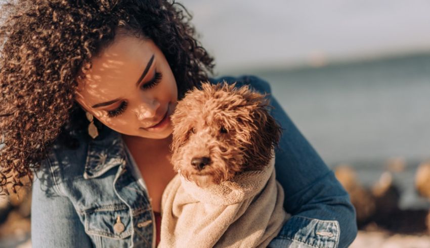 A woman wrapped in a towel with a dog on the beach.