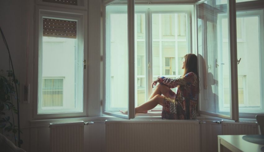 A woman sitting on a window sill looking out.