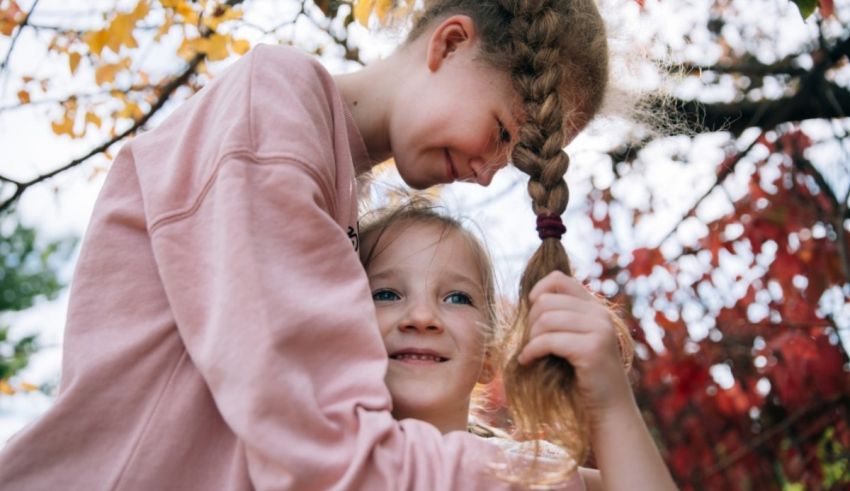 Two girls hugging each other in front of a tree.