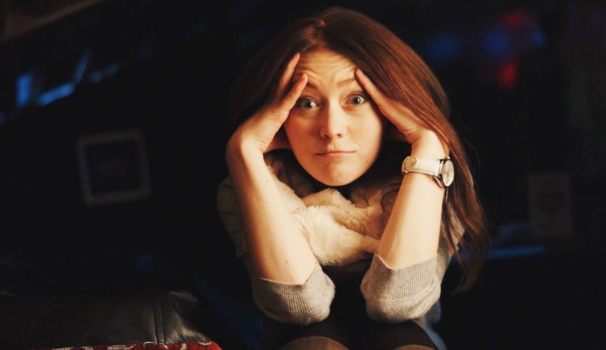 A woman is sitting on a couch with her hands on her head.