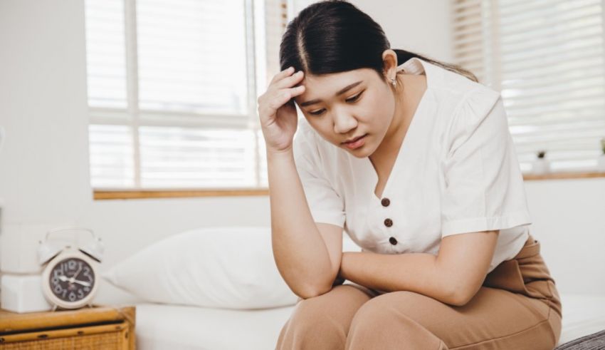 Asian woman sitting on the bed with her hand on her head.