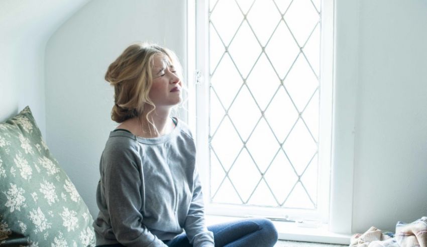A woman sitting in front of a window with her eyes closed.