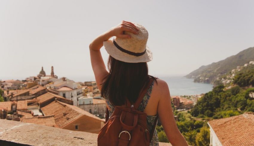 A woman wearing a hat and backpack looking out over the sea.