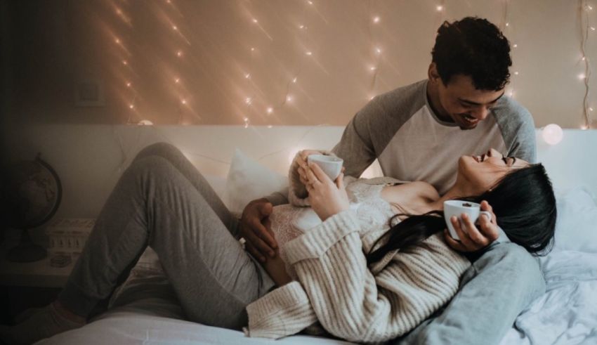 A pregnant couple laying on a bed with lights in the background.