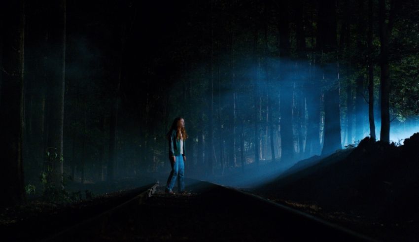 A woman standing on a train track in a dark forest.
