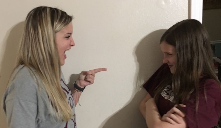 Two girls are pointing at each other in a room.