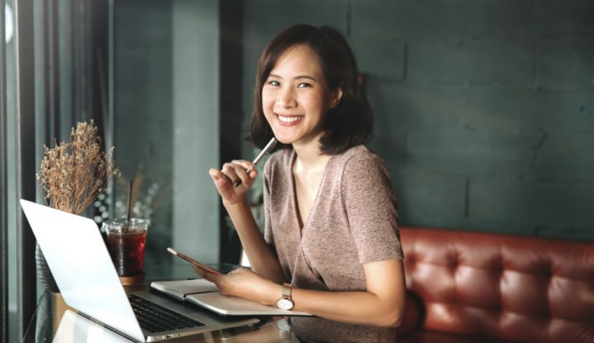 A smiling asian woman sitting at a table with a laptop.