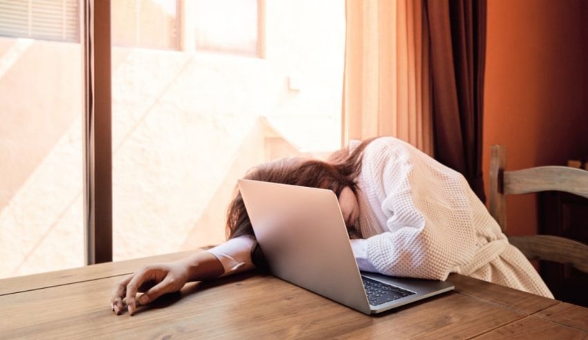 A woman is sleeping on a table with a laptop in front of a window.