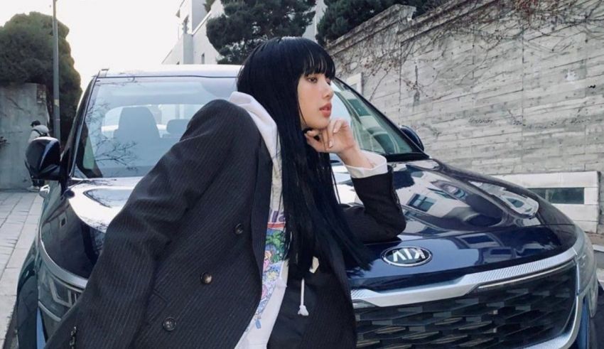 A woman in a suit leaning against a car.