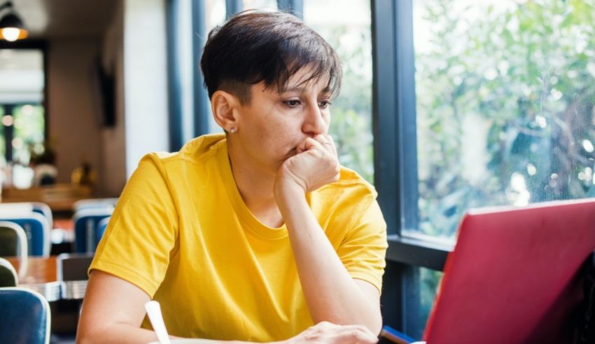 A woman sitting at a table with a laptop in front of a window.