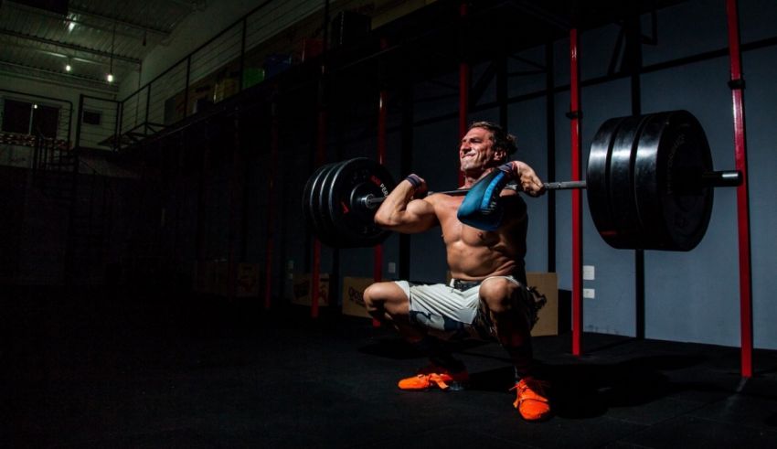 A man squatting with a barbell in a gym.