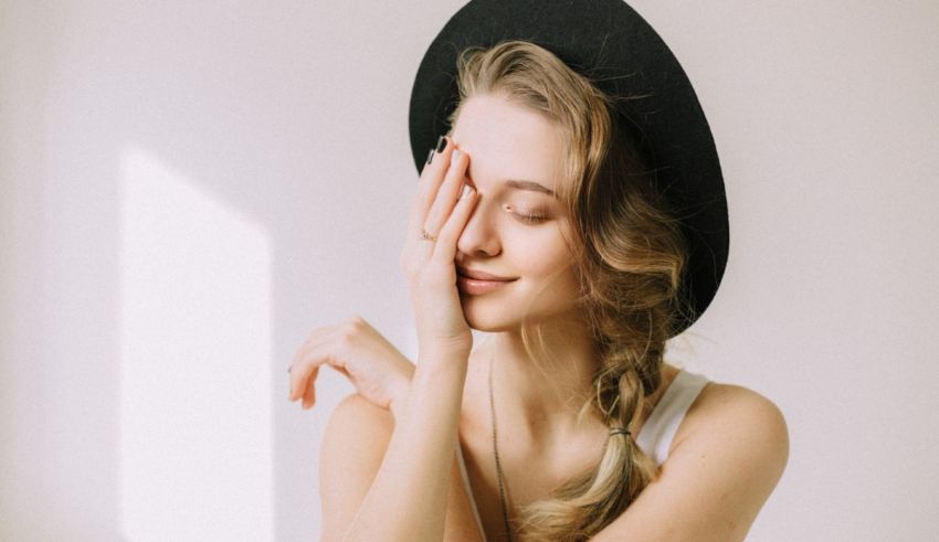 A woman in a black hat covering her face with her hand.