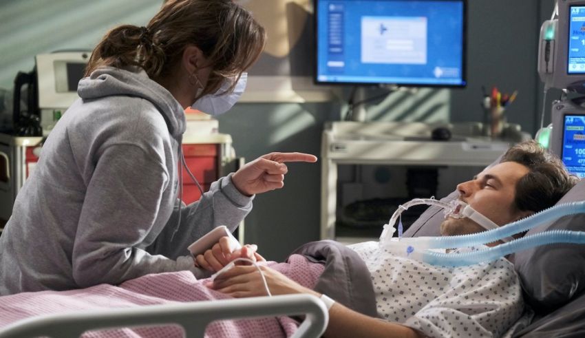 A woman in a hospital bed pointing to a man in a hospital bed.