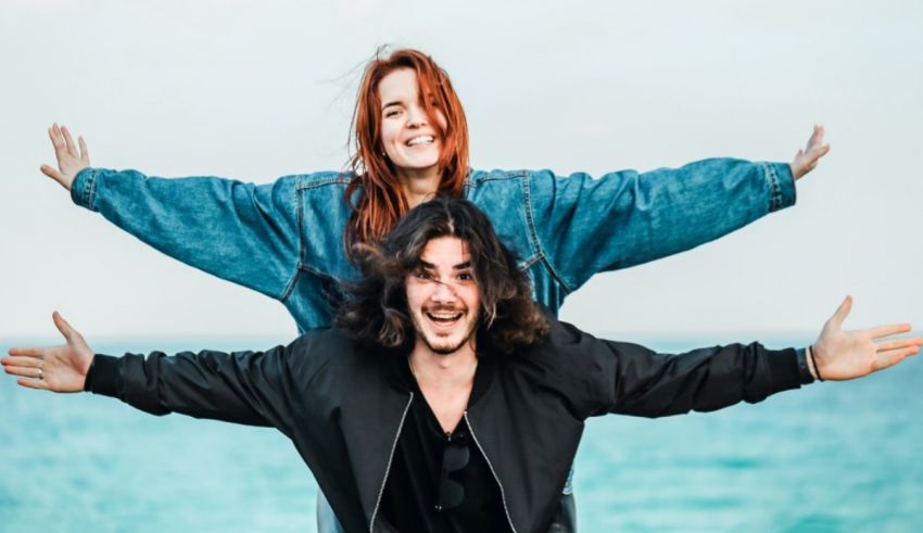 A man and a woman standing on the beach with their arms outstretched.
