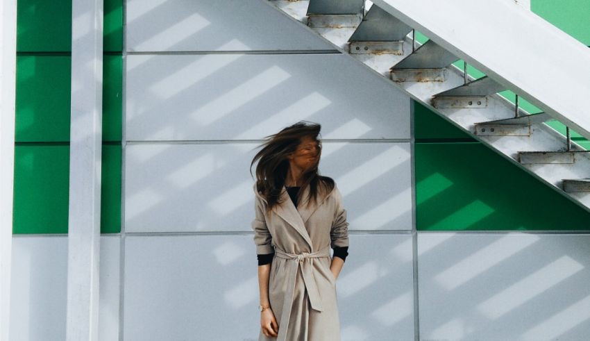 A woman in a trench coat standing next to stairs.