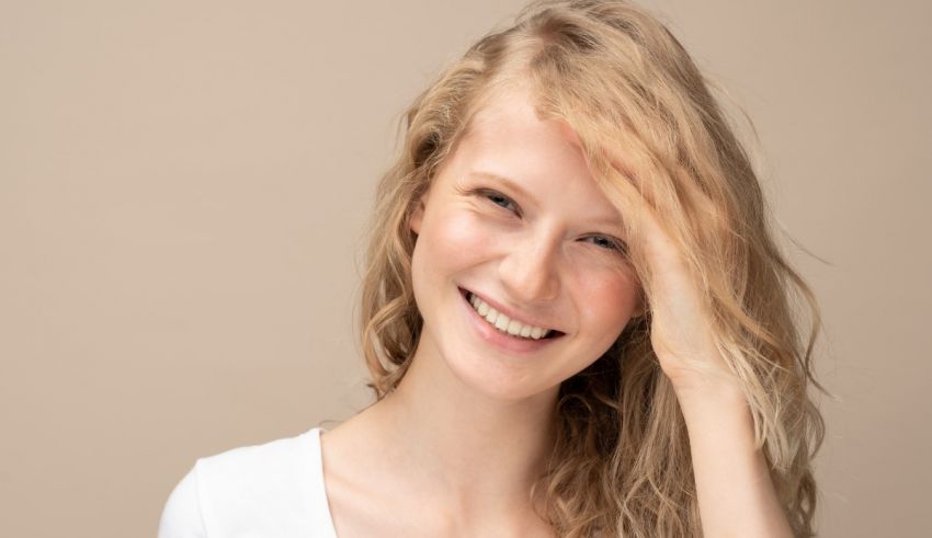 A young woman smiling with her hands on her head.