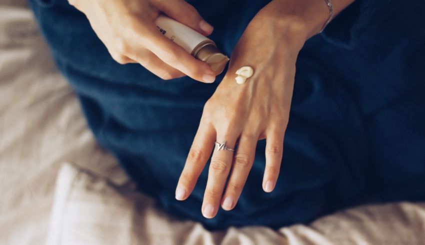 A woman is putting lotion on her hand while sitting on a bed.