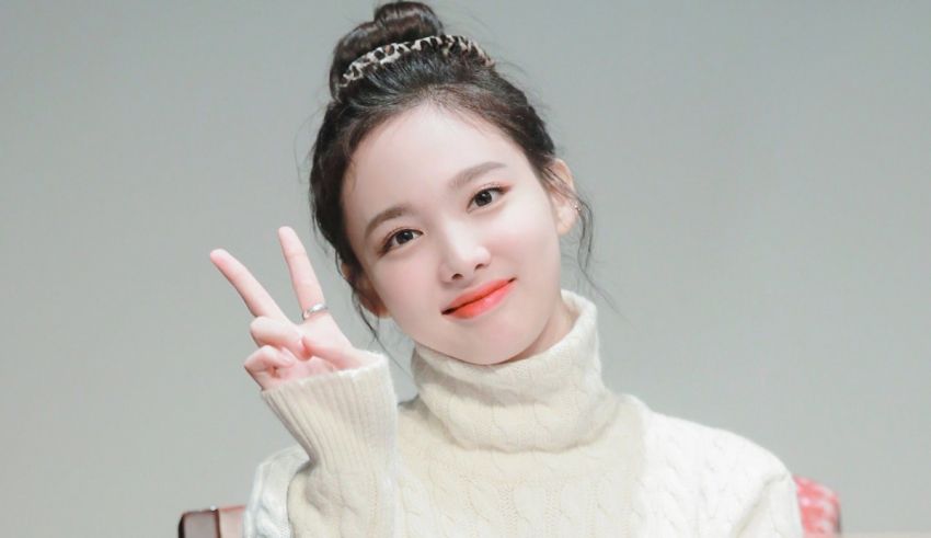 A girl in a white turtleneck sweater making a peace sign.