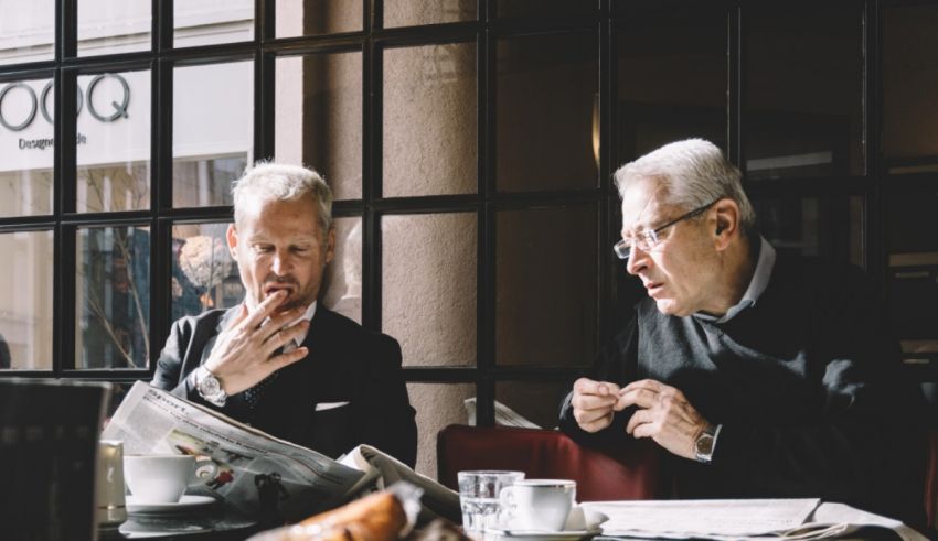 Two men sitting at a table reading a newspaper.