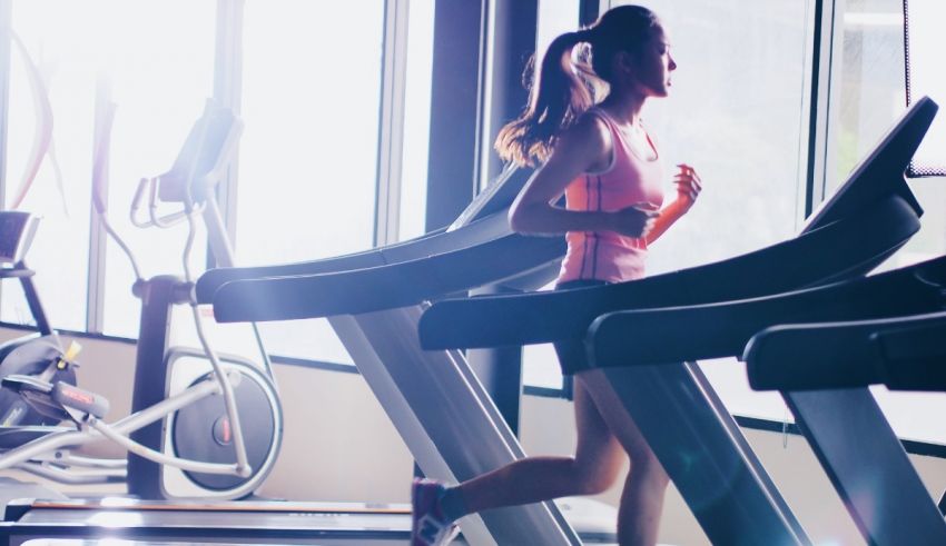 A woman is running on a tread machine in a gym.