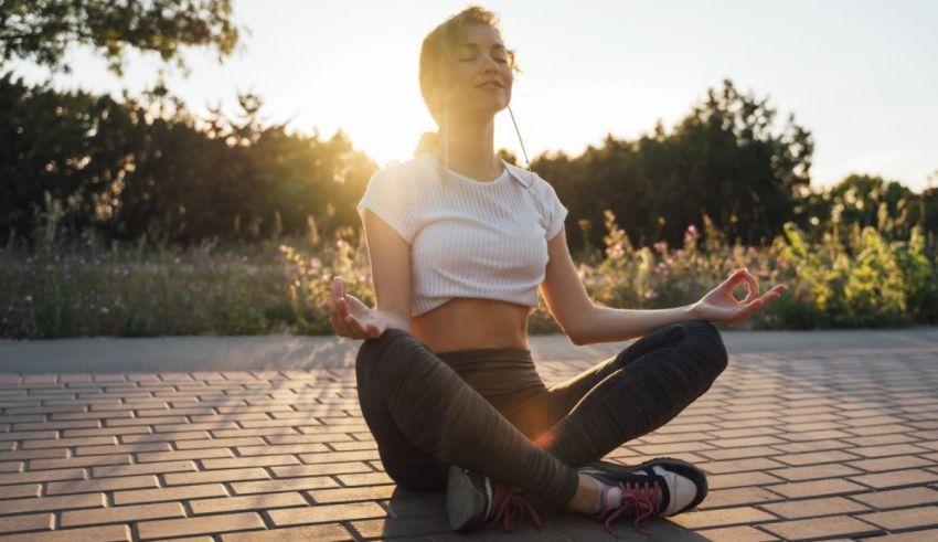 A woman is meditating in a park at sunset.