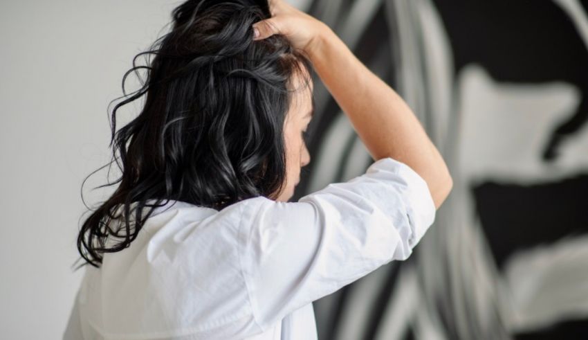 A woman is combing her hair in front of a wall.