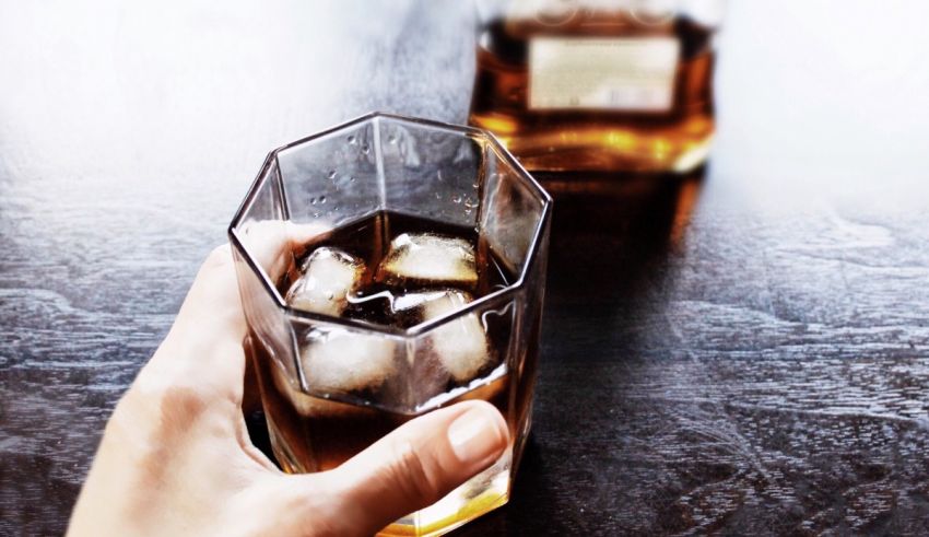 A person holding a glass of whiskey with ice in it.