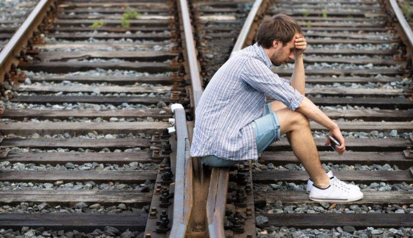 A man sitting on a train track with his head down.