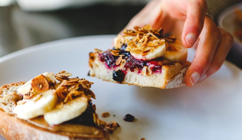 A person is holding a piece of bread with berries and bananas on it.