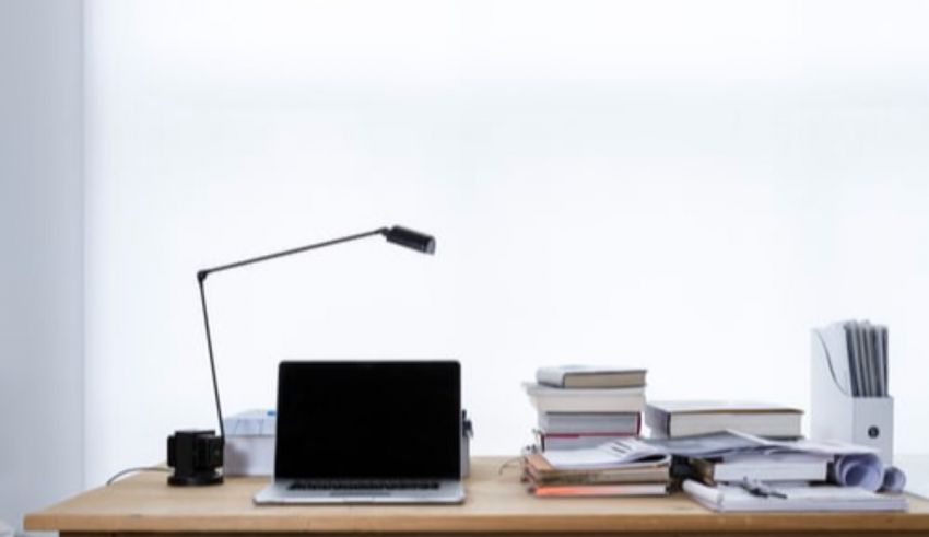 A desk with a laptop, books, and a lamp.