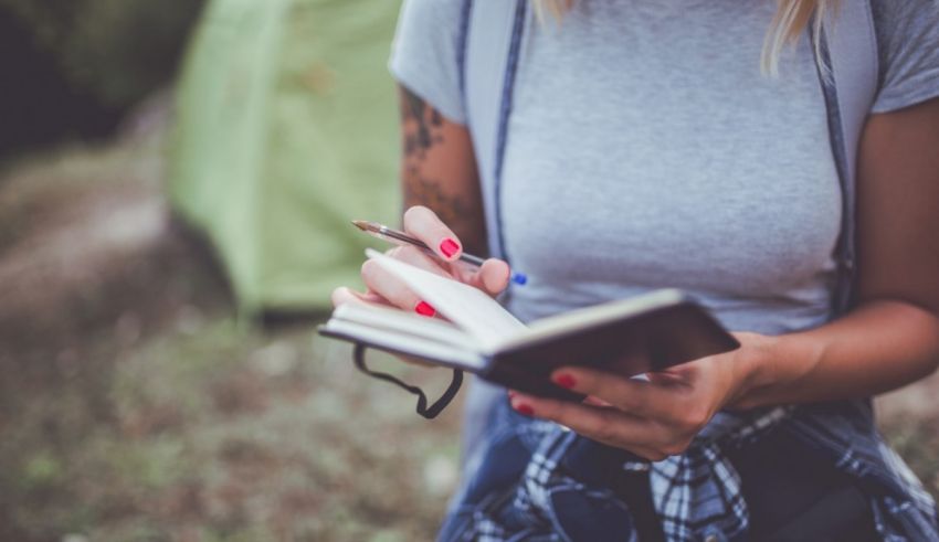 A woman writing in a notebook in front of a tent.