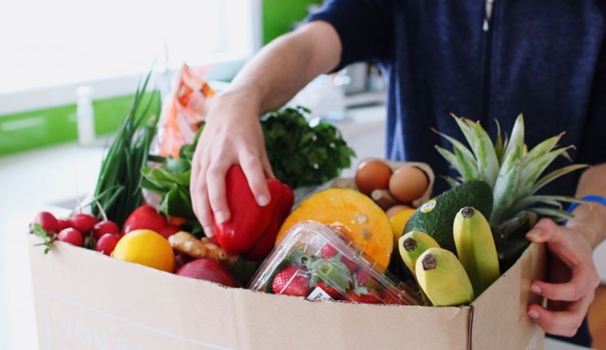 A man is holding a box full of fruits and vegetables.
