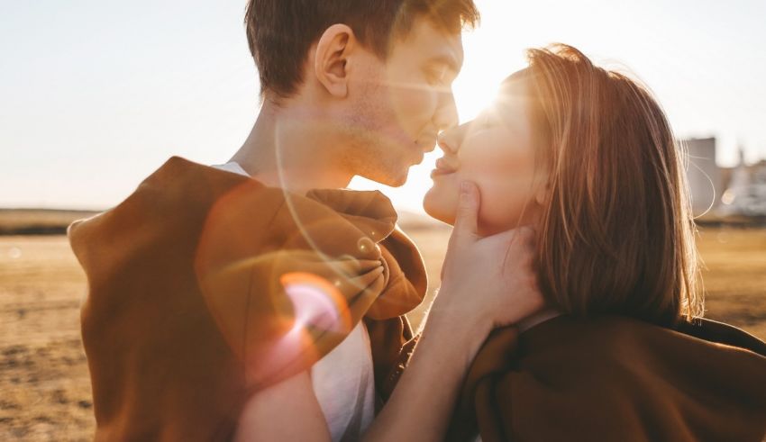 A young couple kissing in a field with the sun behind them.