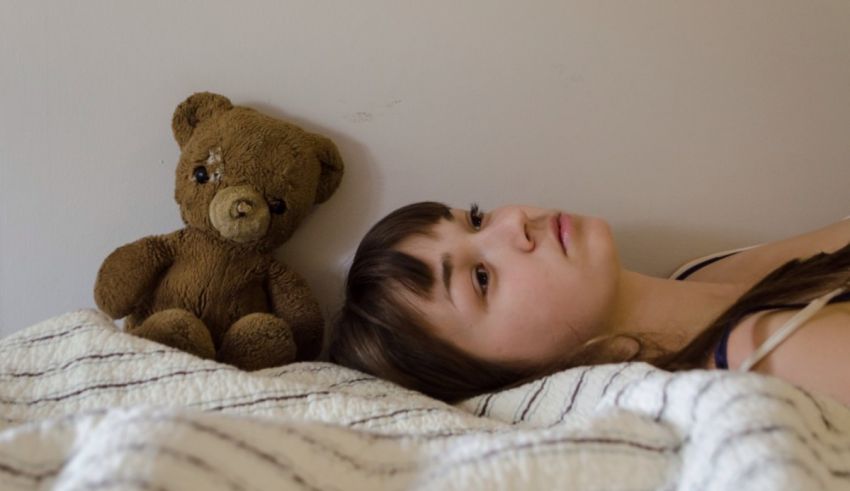 A girl laying on a bed next to a teddy bear.