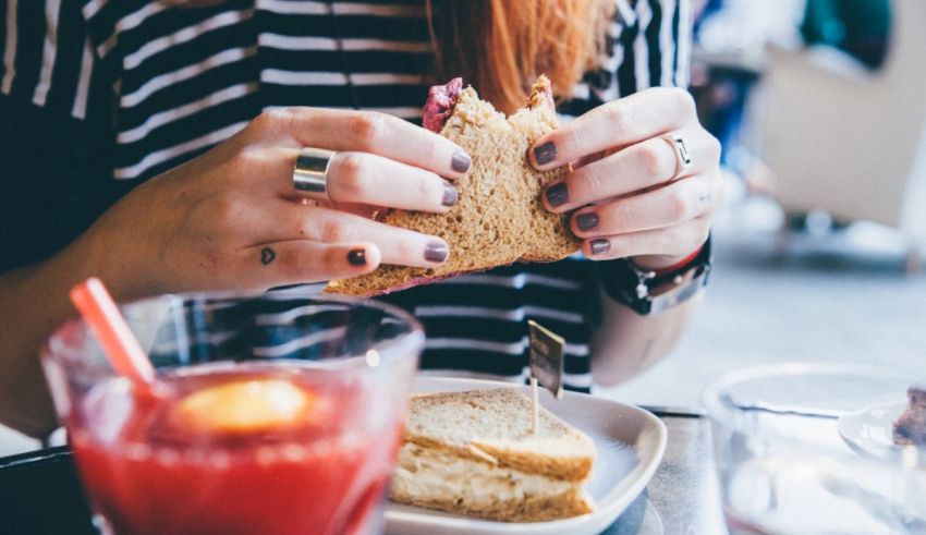 A woman is eating a sandwich with a drink.