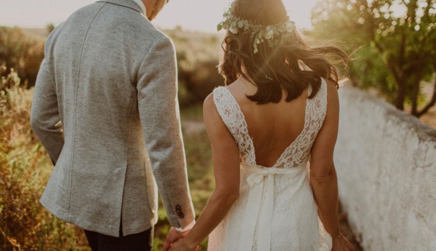 A bride and groom walking through a field at sunset.