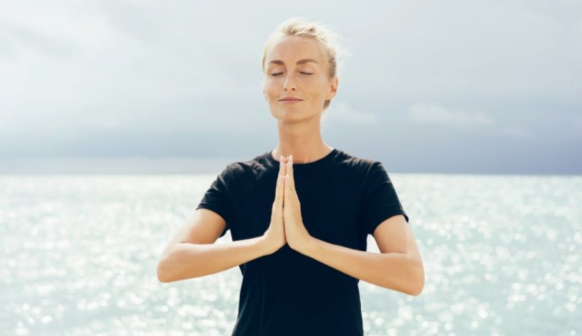 A woman meditating in front of the ocean.