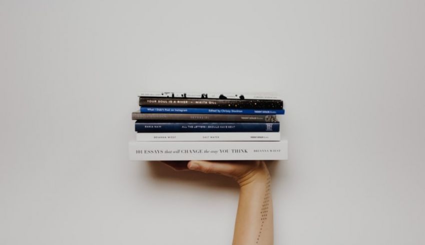A person's hand holding a stack of books.