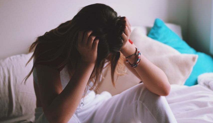 A woman sitting on a bed with her hands on her head.