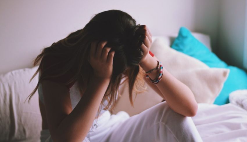 A woman sitting on a bed with her hands on her head.