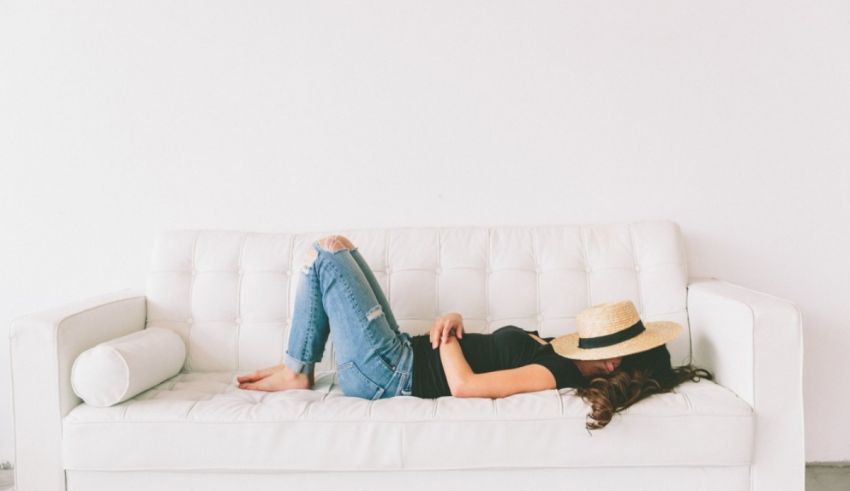 A woman laying on a white couch with a straw hat.