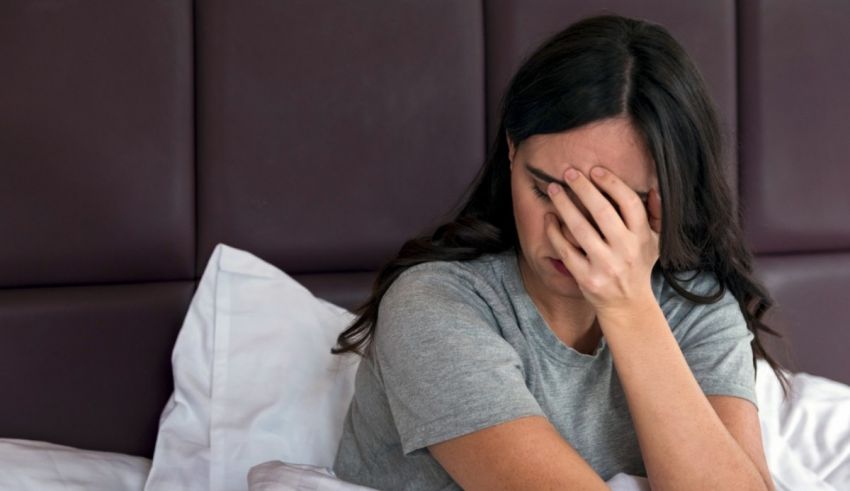 A woman is sitting in bed with her hand on her face.