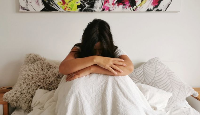 A woman sitting on a bed with her arms wrapped around her head.