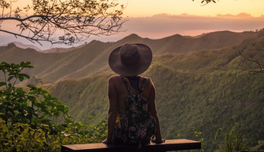 A woman sits on a bench overlooking the mountains at sunset.