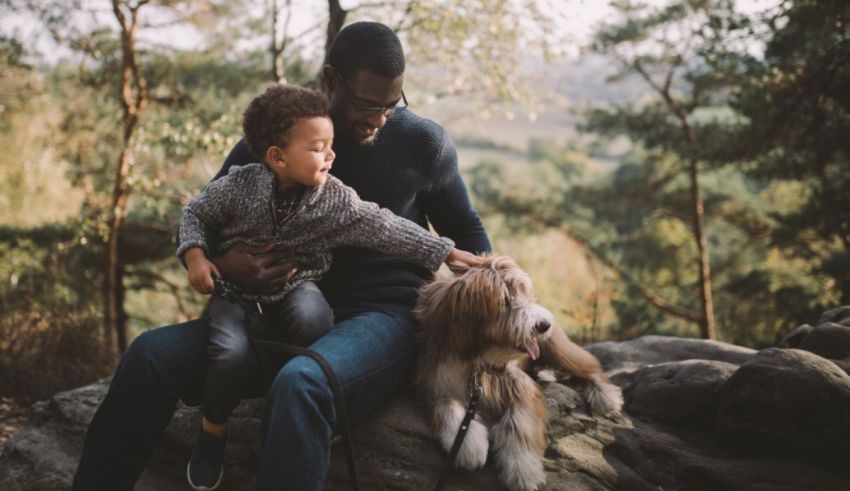 A father and son sitting on a rock with a dog.